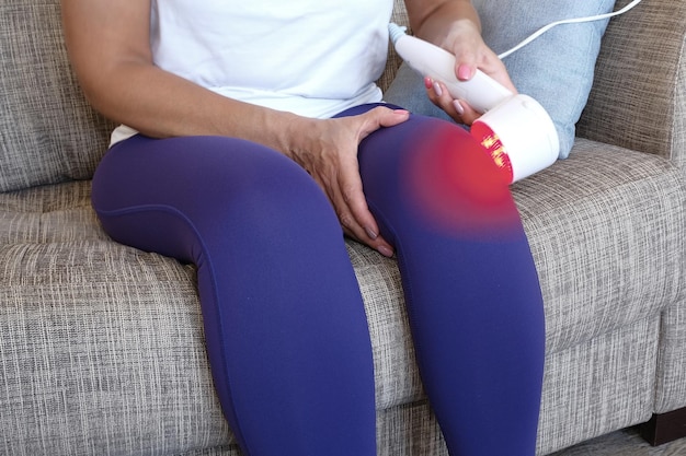 Arthritis is a disease of the joints A woman applies a UHF therapy device sitting on the couch to the knee joint