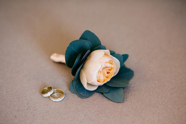 Artificial beige rose and wedding rings lying on white soft background Brides details Composition of brides accessories Gold rings of happy couple going to marry