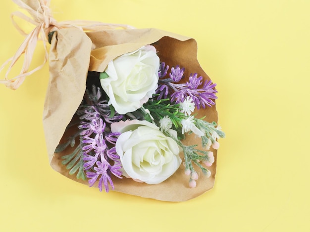 Artificial bouquet of spring flowers in craft paper on a yellow background