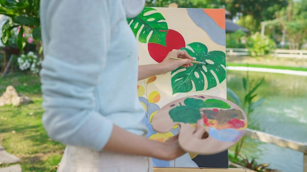 Artist concept Female artist holding color palette and painting picture on canvas in the garden