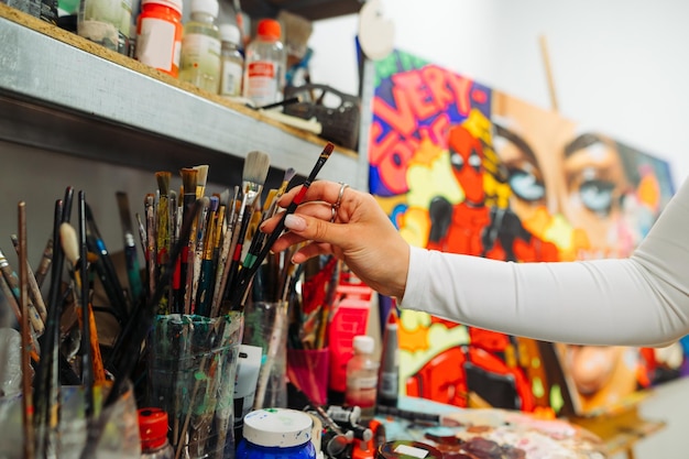 artist hand takes a brush from a brush holder on a painting background artist creates a painting