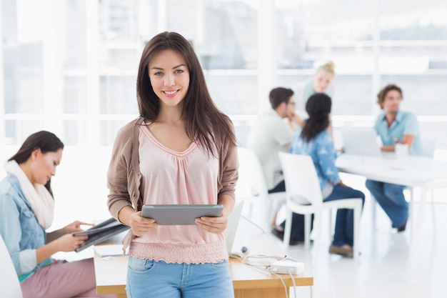 Artist holding digital tablet with colleagues in background at office