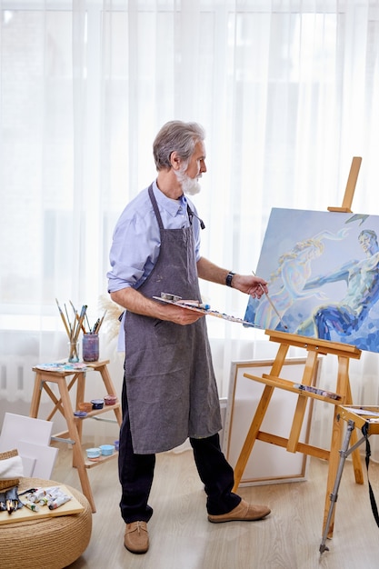 Artist immersed in the creation of art, painting canvas on easel. craftsman in apron enjoy painting, creating masterpiece