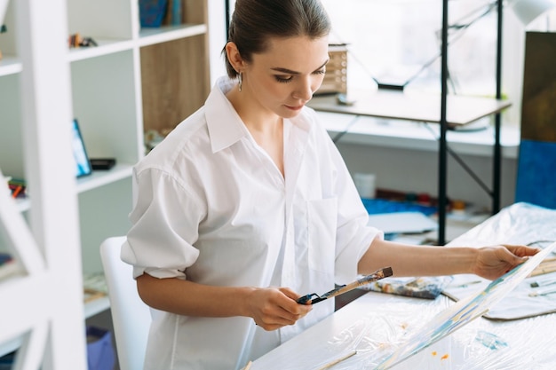 Artist lifestyle Painting art Creative home leisure Talented satisfied painter woman in white shirt with paintbrush tools picture in modern light workshop