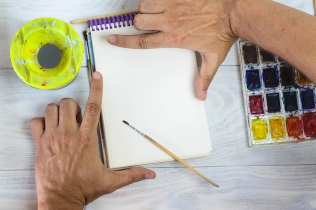 The artist's hands paint palette brushes different colors The man is drawing The artist's tools for real art and inspiration Top View