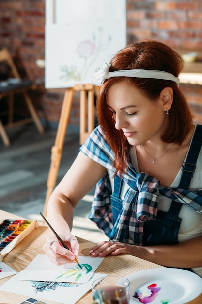 Artist studio. Watercolor painting creation. Redhead female doing sketch brushstrokes getting inspiration.