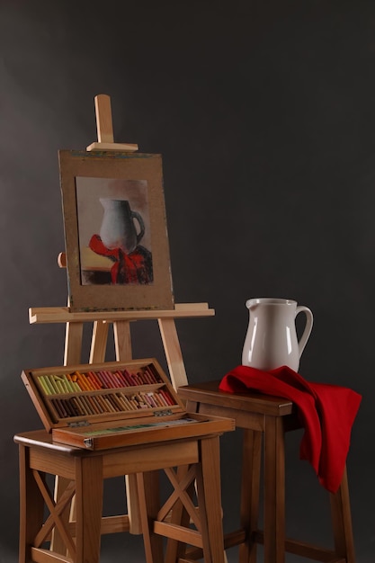 Artist39s workplace with easel drawing and soft pastels against black background