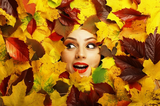 Artistic conceptual autumn girl portrait. Colorful leaves. Leaves of trees around an emotional face. Autumn is coming.