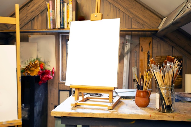 Artistic equipment in a artist studio empty artist canvas on wooden easel and paint brushes retro to...