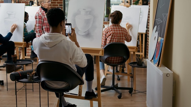 Artistic person taking photo of vase masterpiece on canvas. Art class student using smartphone to take picture of sketch after finishing drawing model, saving contemporary masterpiece.