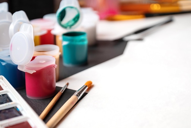 Artistic work desk with plastic gouache paint cans paint brushes and paper ready to draw