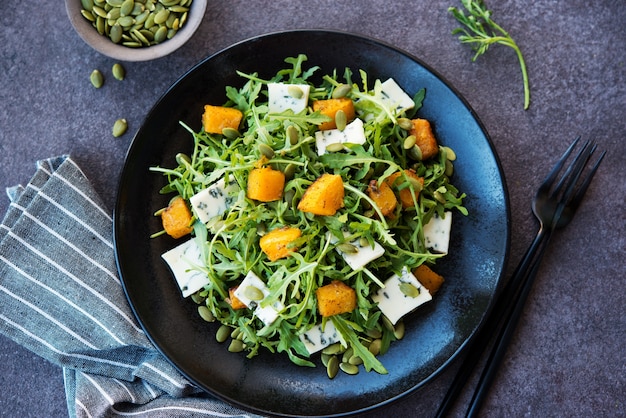 Arugula, blue cheese, pumpkin, pumpkin seeds, salad in a plate, top view