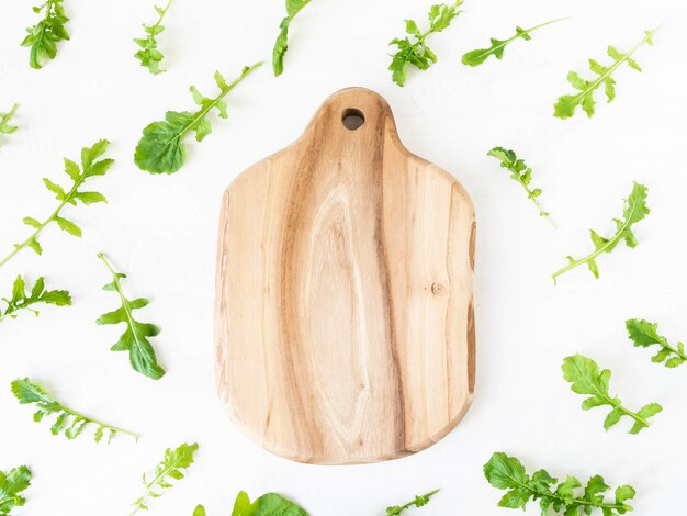 Arugula pattern isolated on white background. Composition made of arugula leaves and wood cutting board. Flat lay, top view