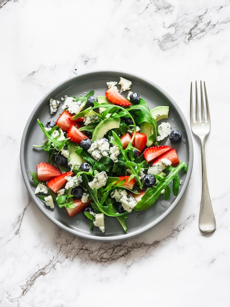 Arugula strawberry gorgonzola avocado salad on a light background top view