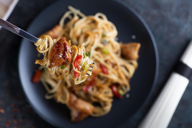 Asia food Udon stirfry noodles with chicken meat and sesame in bowl on dark stone background copy