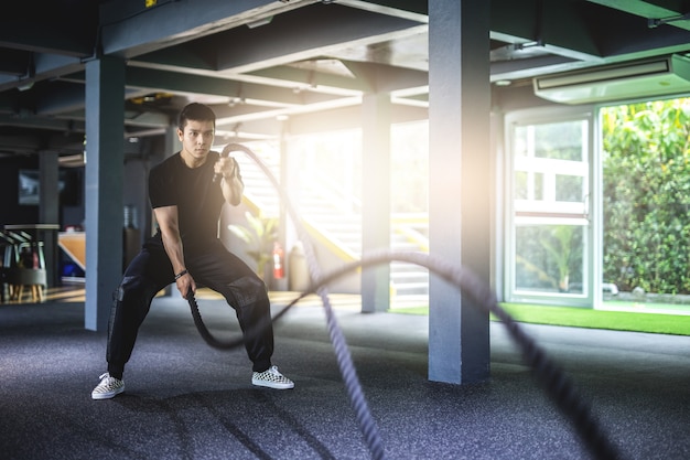 Asia man exercising with battle ropes at gym.