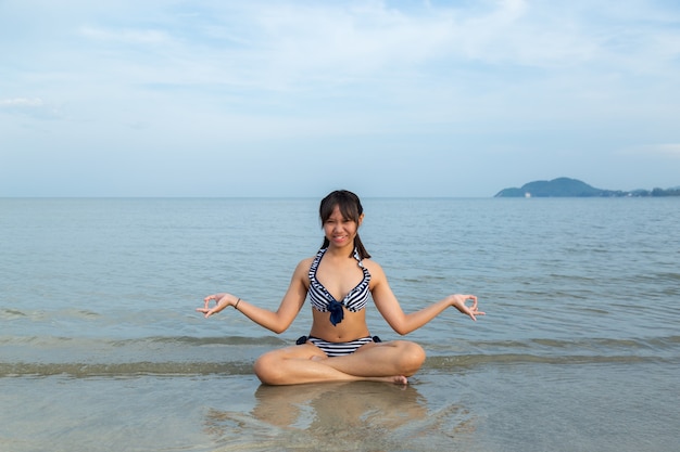 Asia teenage girls wearing bikini sitting meditation at the beach.