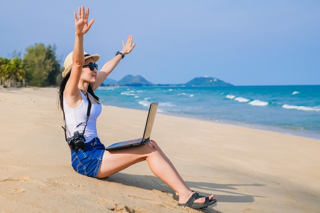 Asia woman sitting on the beach and using laptop for her work and checking business during her vacation.