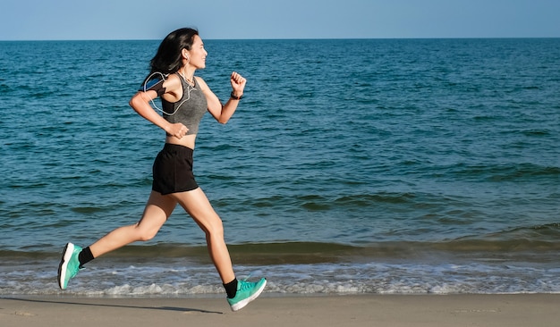 Asia woman in sport ware exercising and running on the beach.