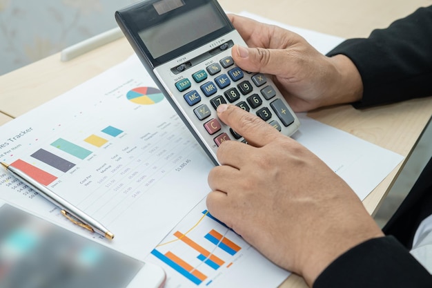 Asian accountant working and analyzing financial reports project accounting with chart graph and calculator in modern office, finance and business concept.