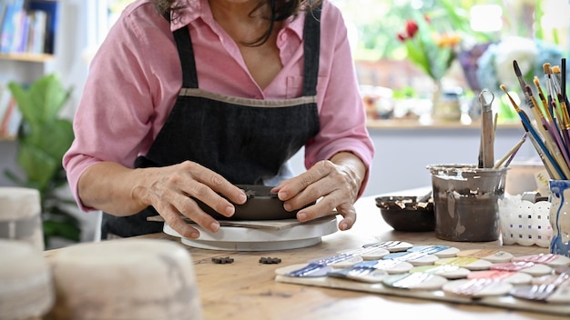 Asian aged woman making a clay ceramic plate on the table cropped image