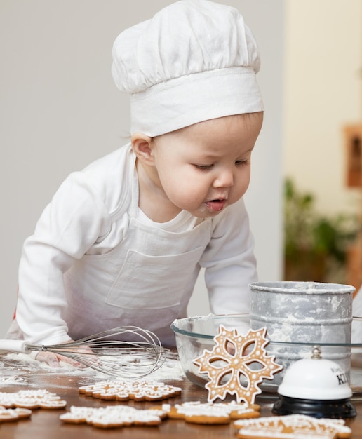 An Asian baby in a chef's cap and apron smeared in flour prepares Christmas ginger cookies