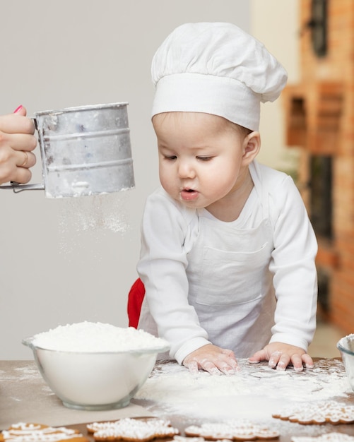 An Asian baby in a chef's cap and apron smeared in flour prepares Christmas ginger cookies