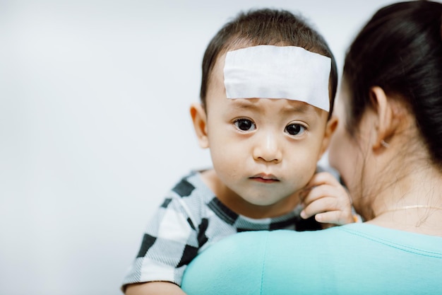 Asian baby feverish and crying His mother relieves heat with a cooling fever gel pad on the forehead Baby illnessUnhappy baby Selective focus