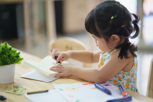 Asian baby girl drawing with colourful crayon happy funny child girl and mom draws laughing training development abilities childs art concept