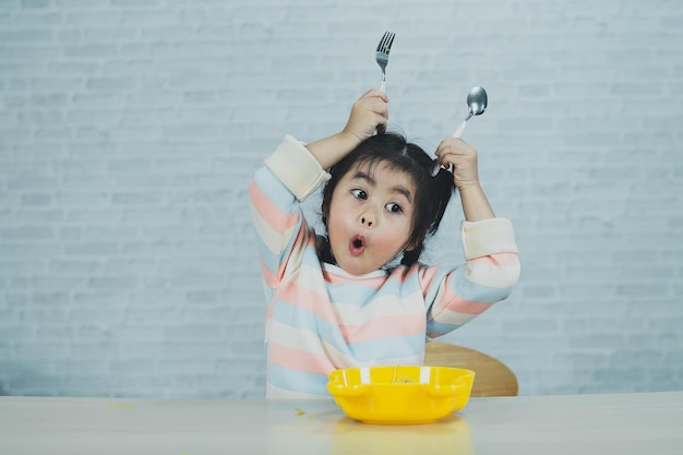 Asian baby girl enjoy happy using cutlery spoon and fork eating delicious noodle in kitchen on dining table Happy asian baby girl practice eating by her self on dining table Baby food concept