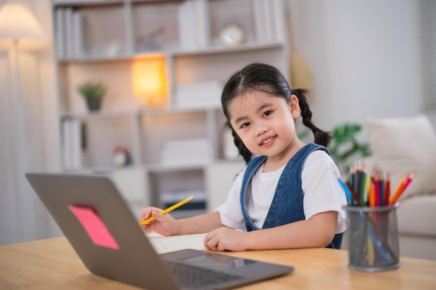 Asian baby girl smiling use laptop or writing drawing color on note book study online on wood table desk in living room at home Education learning online from home concept