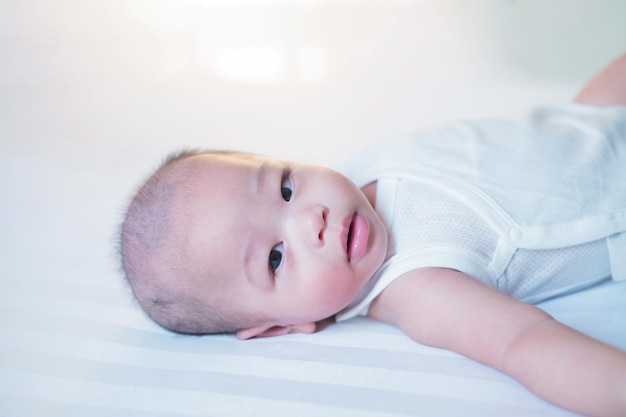 Asian baby in white is sleeping on the bed