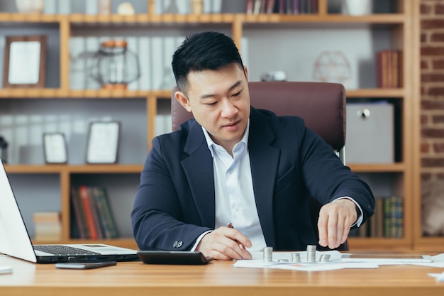 An Asian banker works in a classic office at a table counting coins made of precious metals