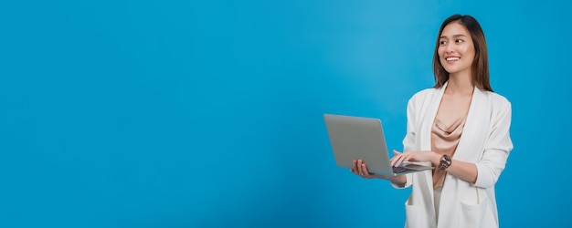 Asian beautiful businesswoman holding laptop in blue colour background with copy space.Concept of online business success with technology.