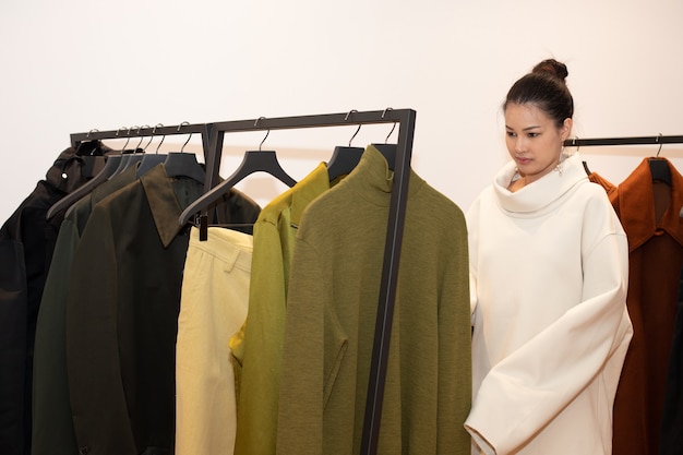 Asian Beautiful Woman in dress select new collection on white orange green earth tone clothes rack in retail fashion store which just open brand news for winter autumn as minimal style