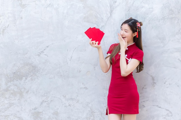 Asian beautiful woman in red dress stands and holds a red envelope with an excited expression