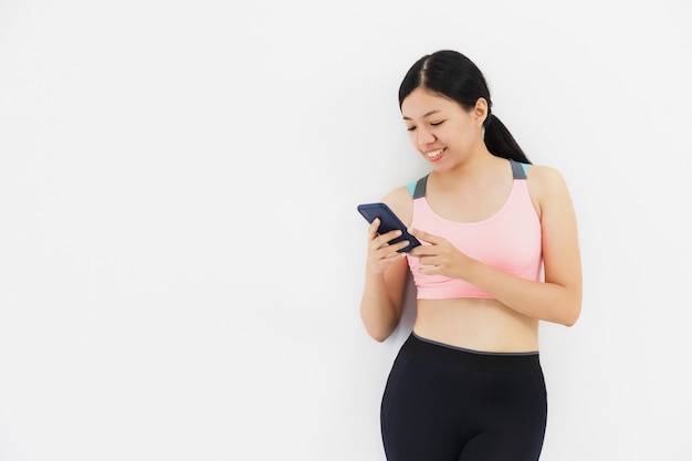 Asian beautiful women using smartphone after play yoga and exercise on white wall 