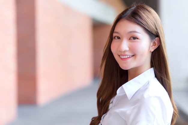 Asian beautiful young woman student is smiling and looking at camera in university background