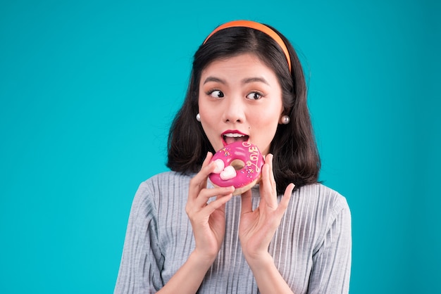 Asian beauty girl holding pink donut. Retro joyful woman with sweets, dessert standing over blue background.