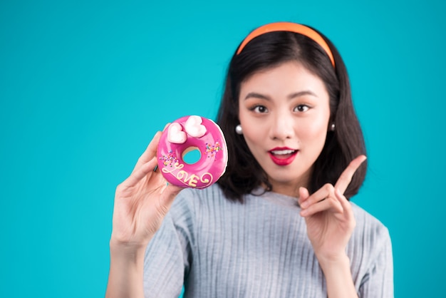 Asian beauty girl holding pink donut. Retro joyful woman with sweets, dessert standing over blue background.