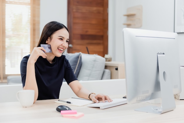 Asian beauty woman use a credit card to make purchases using a computer through the internet With a happy smiling face, being a new normal online business In the shopping experience from home.