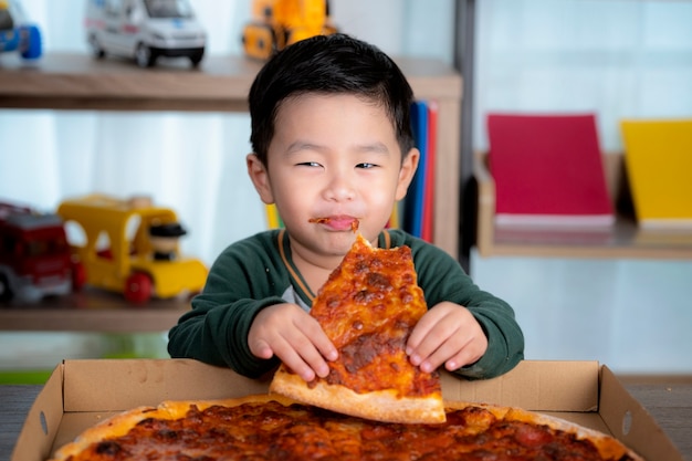 Asian boy eating pizza and pizza box put on the table.