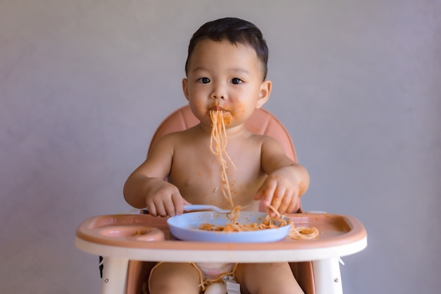 Asian boy eatting on high baby chair.