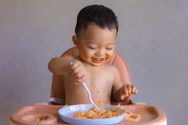 Asian boy eatting on high baby chair.