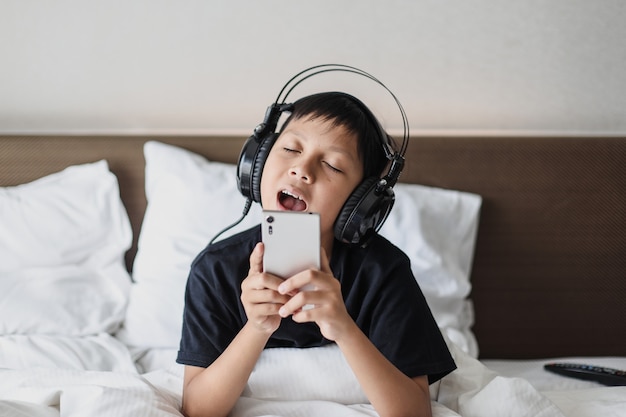 Asian boy in headphone listening music from smart phone while singing on the bed