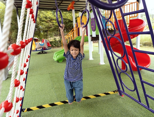 Asian boy is climbing on a playground equipment in a school.