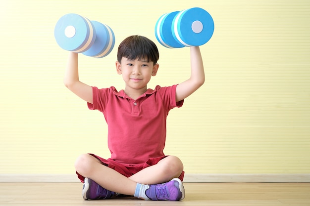 Asian boy is sitting and dumbbells lifting with both hands and face is smiling