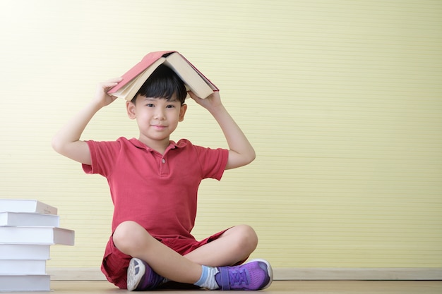 Asian boy is sitting and has a book on his head. Children's learning concept.