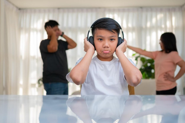 Asian boy kid wearing headphones and play loud music so as not to hear quarrel while parents