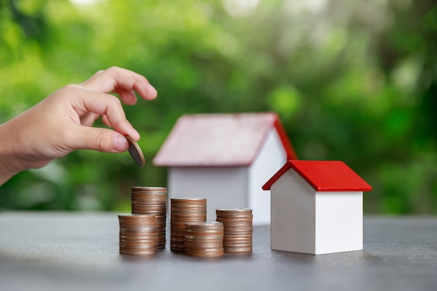 Asian boy putting money to coin stack with house model on green.